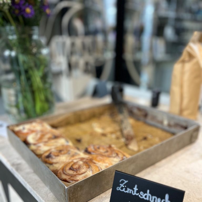 Auf dem Bild ist ein Blech mit leckeren Zimtschnecken, ein Blumenstrauß im Hintergrund auf der Bar im MANANA coffee shop in Wien